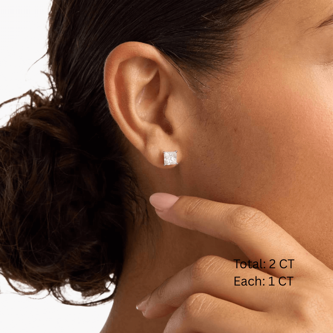 Princess-cut moissanite stud earrings worn on the ear, 2 ct per pair with 1 ct per stone.