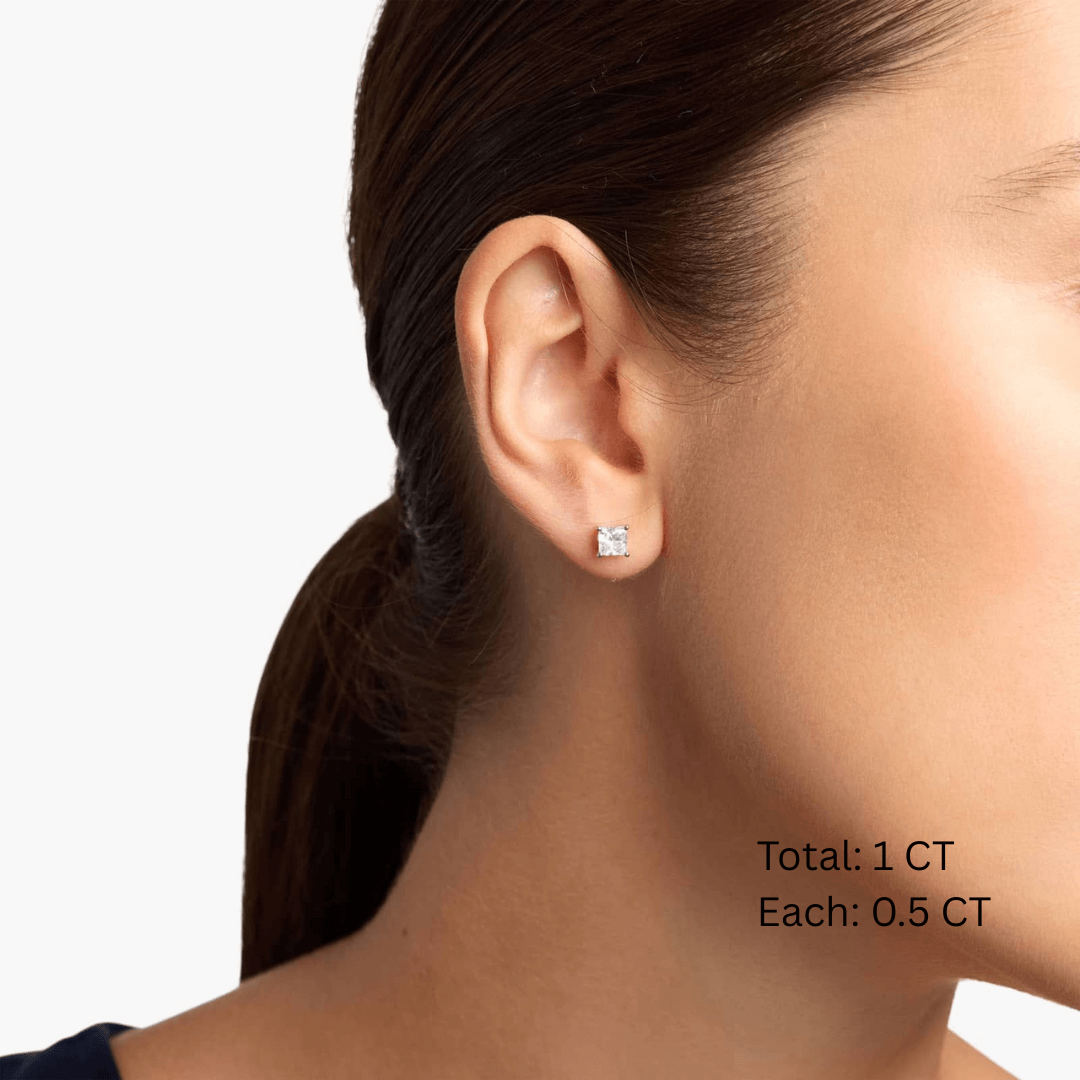 Princess-cut moissanite stud earrings worn on the ear, 1 ct per pair with 0.5 ct per stone.