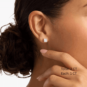 Princess-cut moissanite stud earrings worn on the ear, 2 ct per pair with 1 ct per stone.