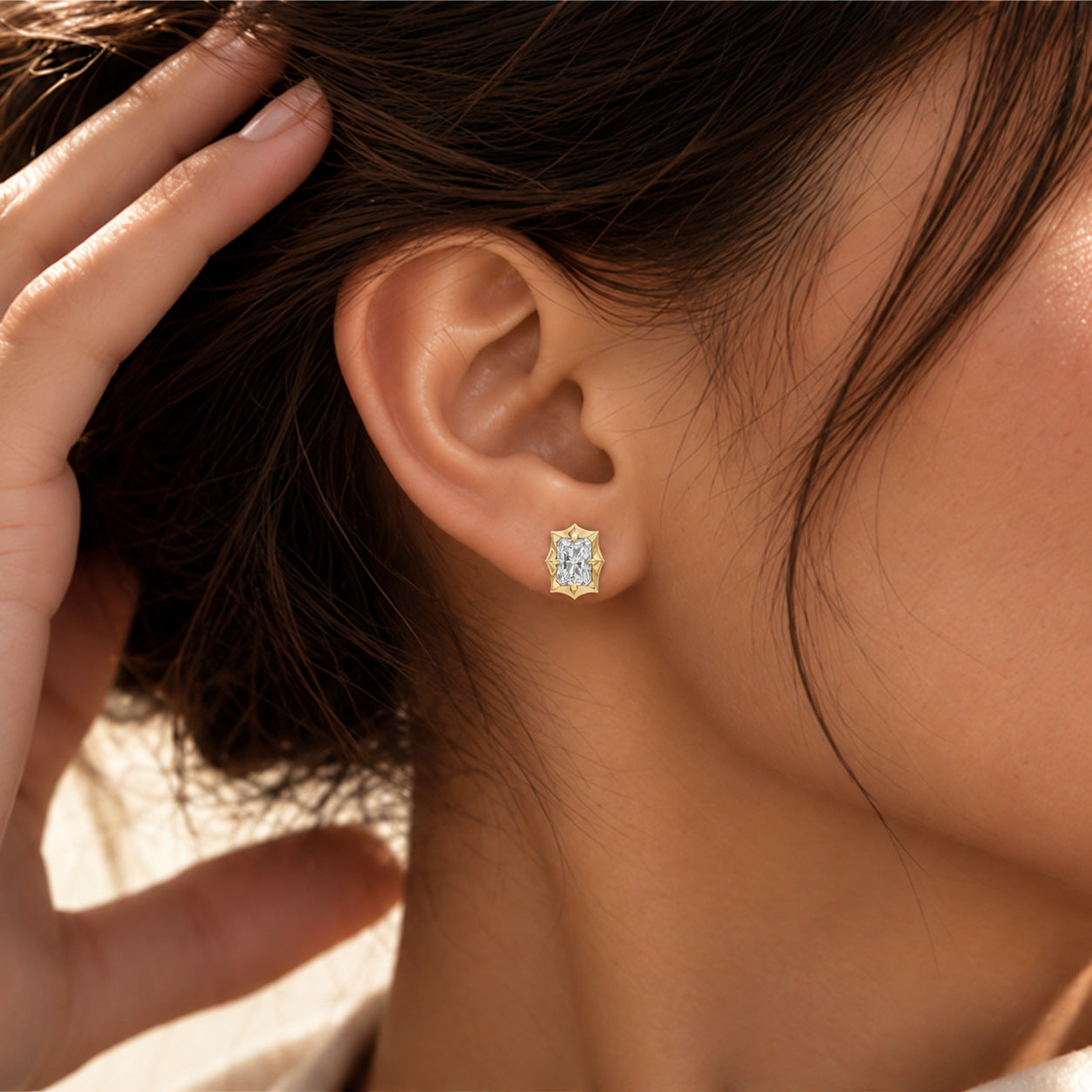 Close-up of a model wearing a radiant-cut moissanite bezel-prong stud earring in 18k yellow gold vermeil.