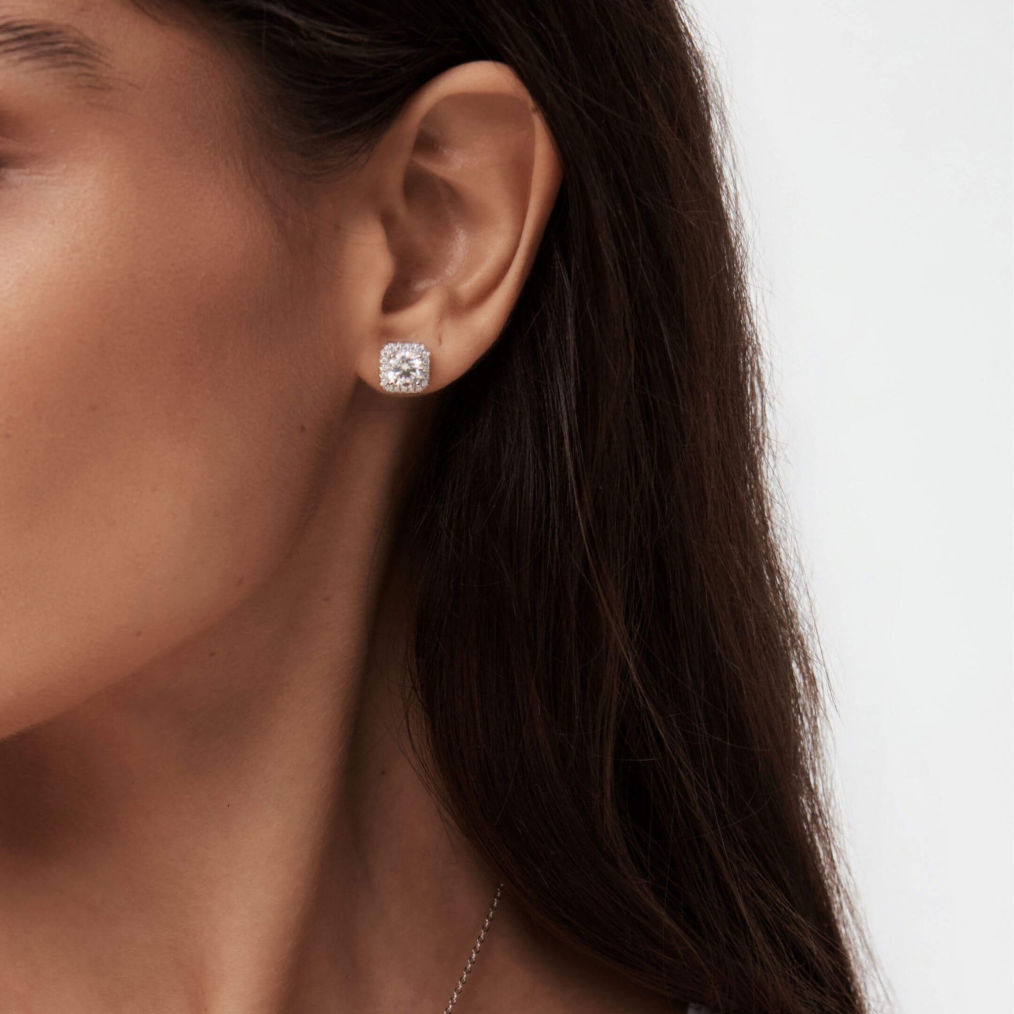 Round-cut moissanite cushion halo stud earrings worn on the ear.