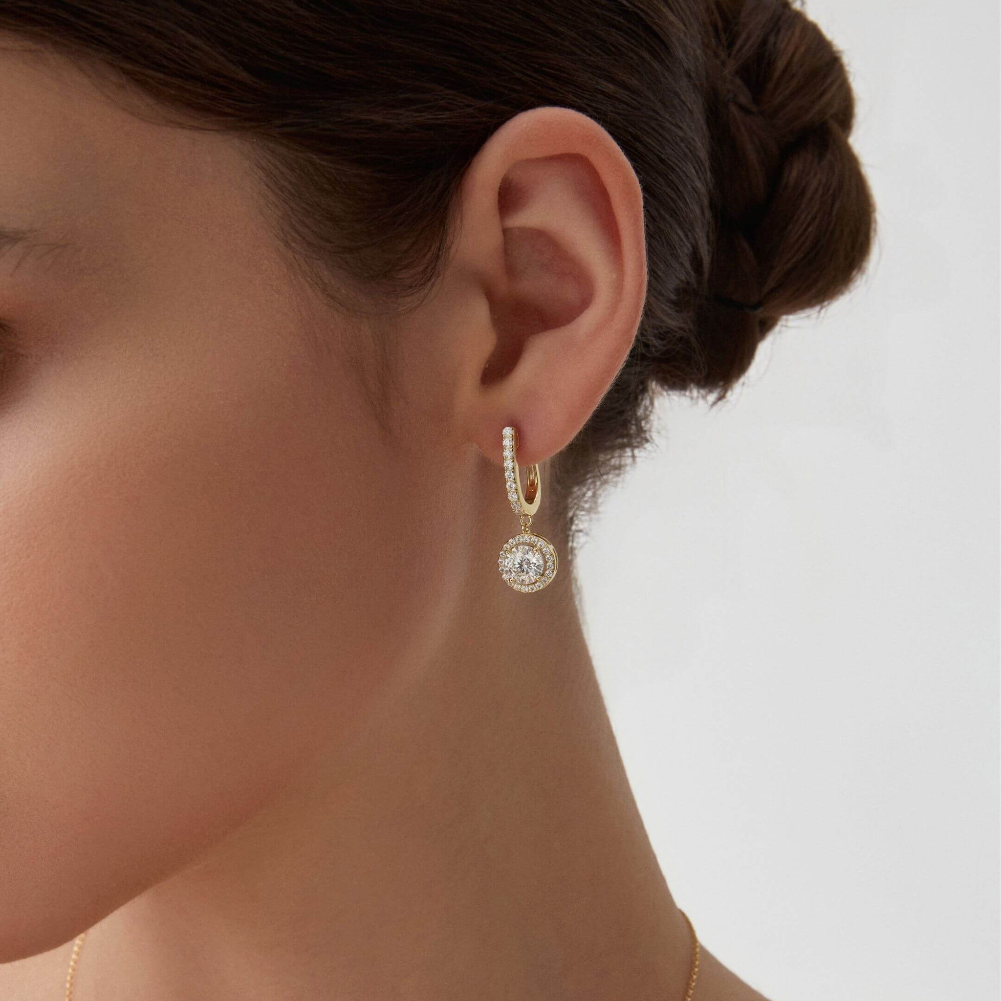 Round-cut moissanite halo drop earrings worn on the ear.