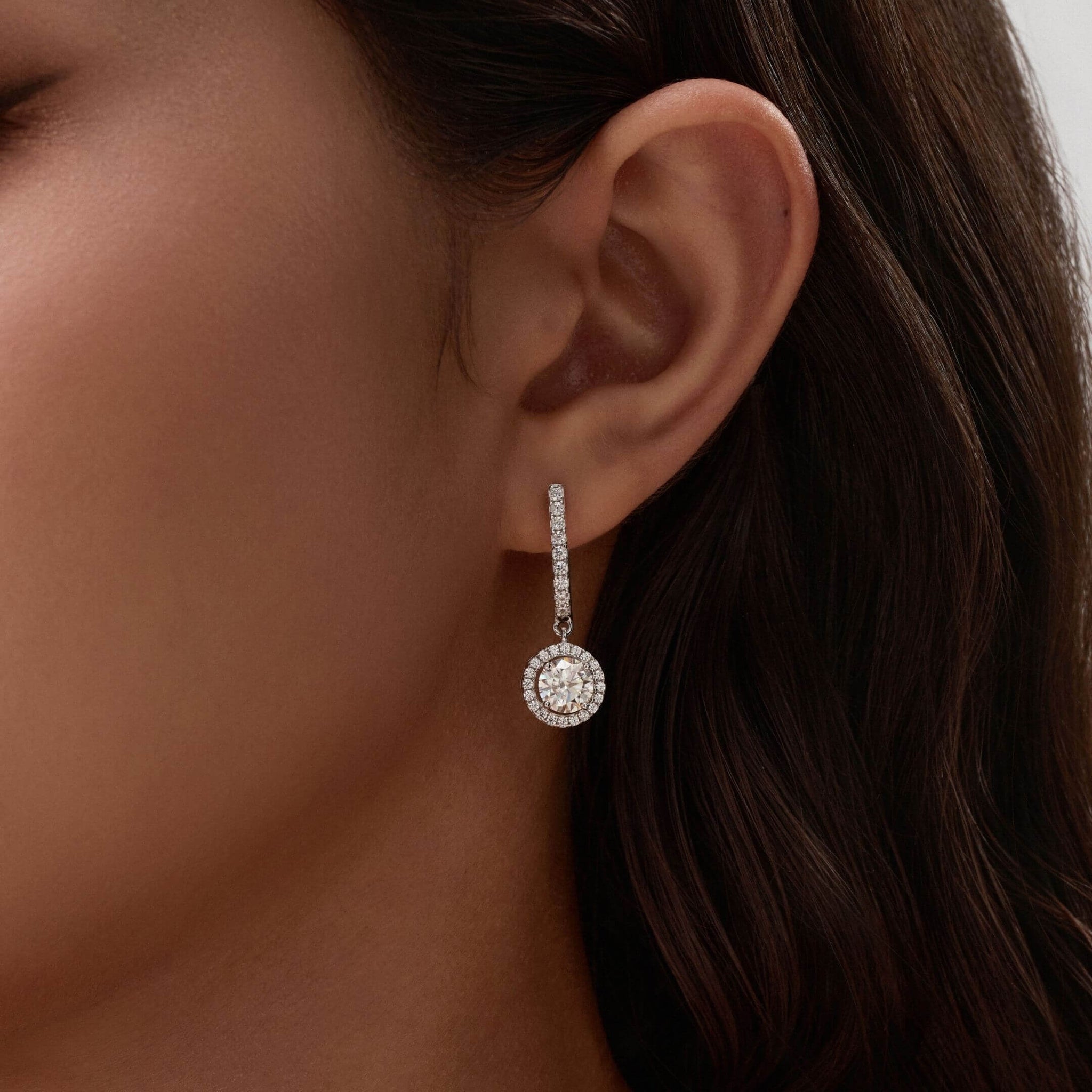 Round-cut moissanite halo drop earrings worn on the ear.