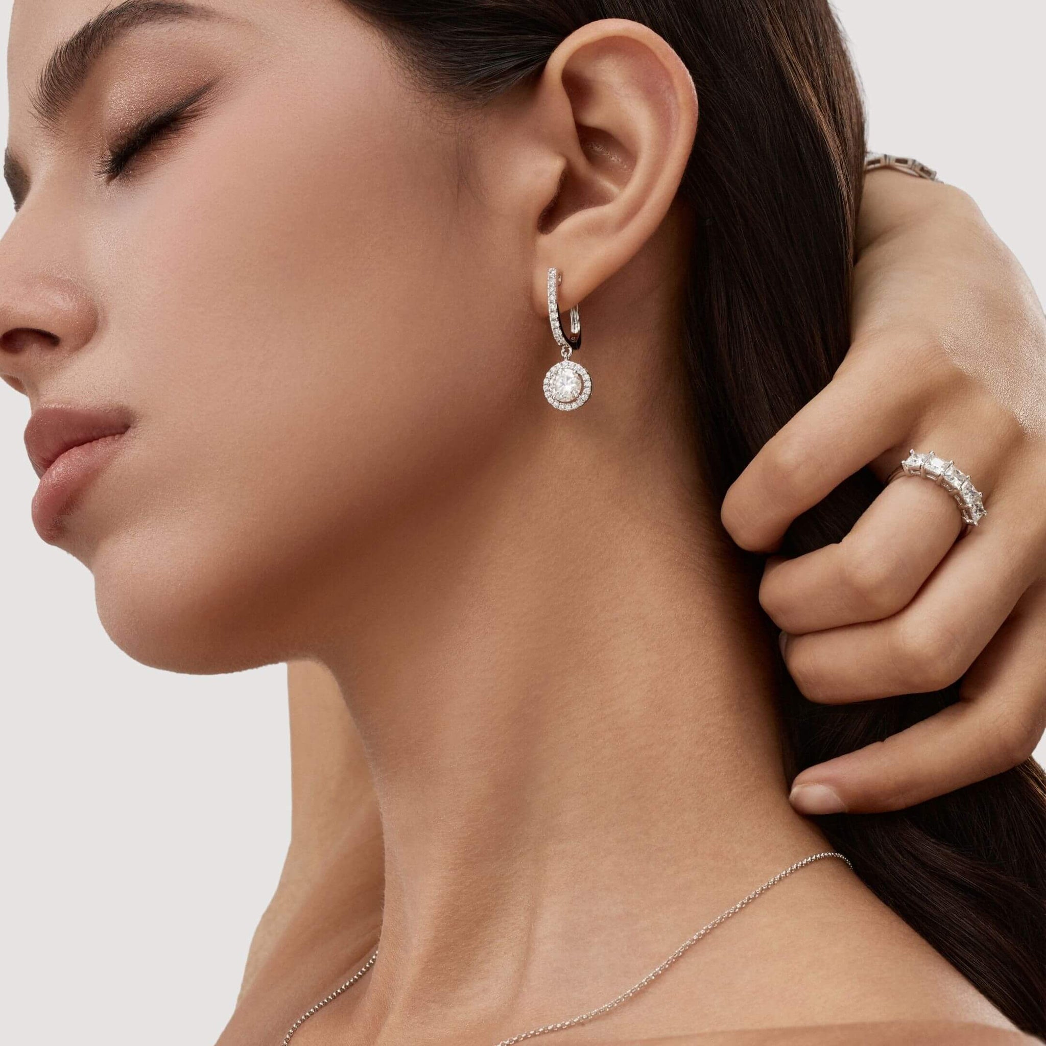 Round-cut moissanite halo drop earrings worn on the ear.