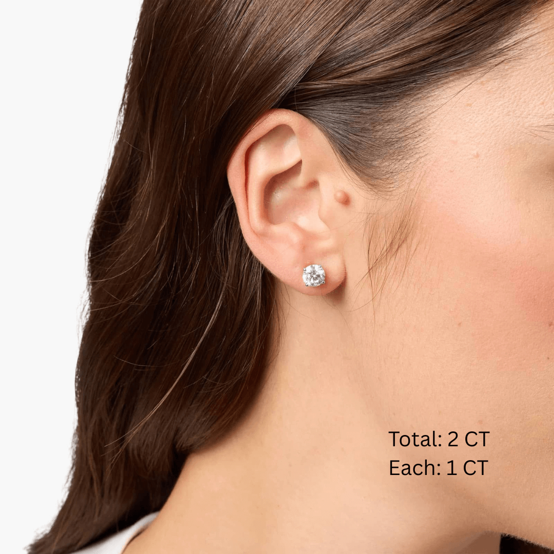 Round-cut moissanite stud earrings worn on the ear, 2 ct per pair with 1 ct per stone.