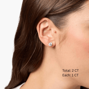 Round-cut moissanite stud earrings worn on the ear, 2 ct per pair with 1 ct per stone.