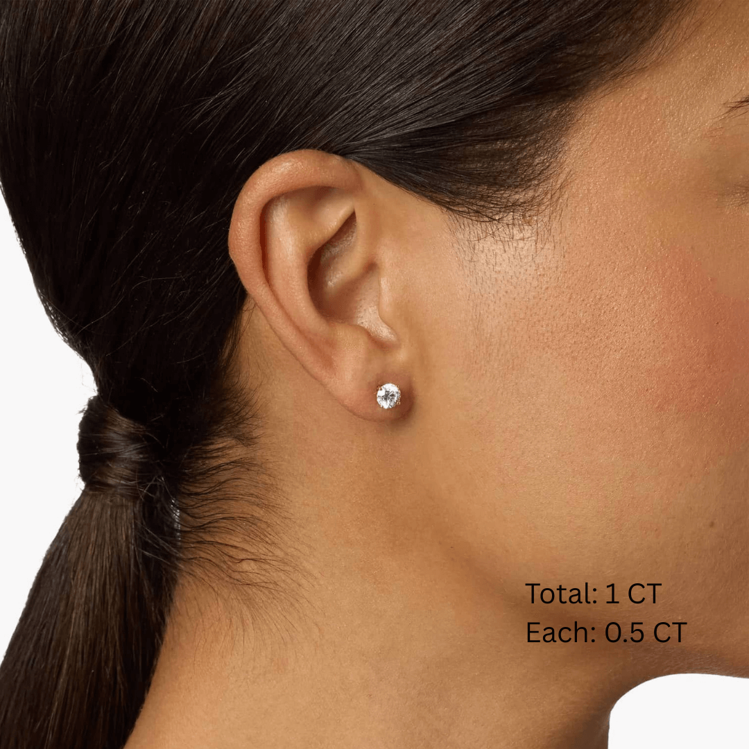Round-cut moissanite stud earrings worn on the ear, 1 ct per pair with 0.5 ct per stone.