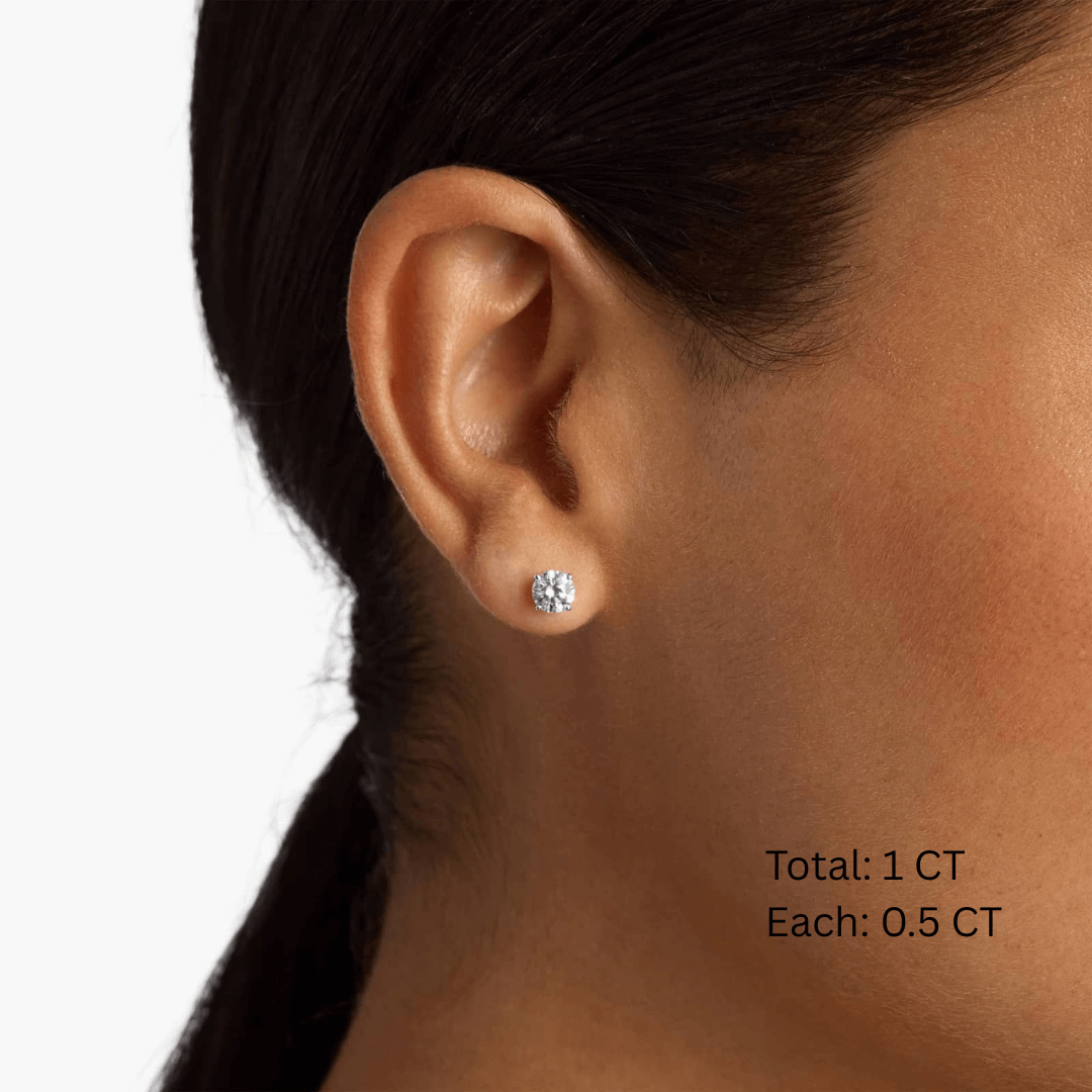 Round-cut moissanite stud earrings worn on the ear, 1 ct per pair with 0.5 ct per stone.