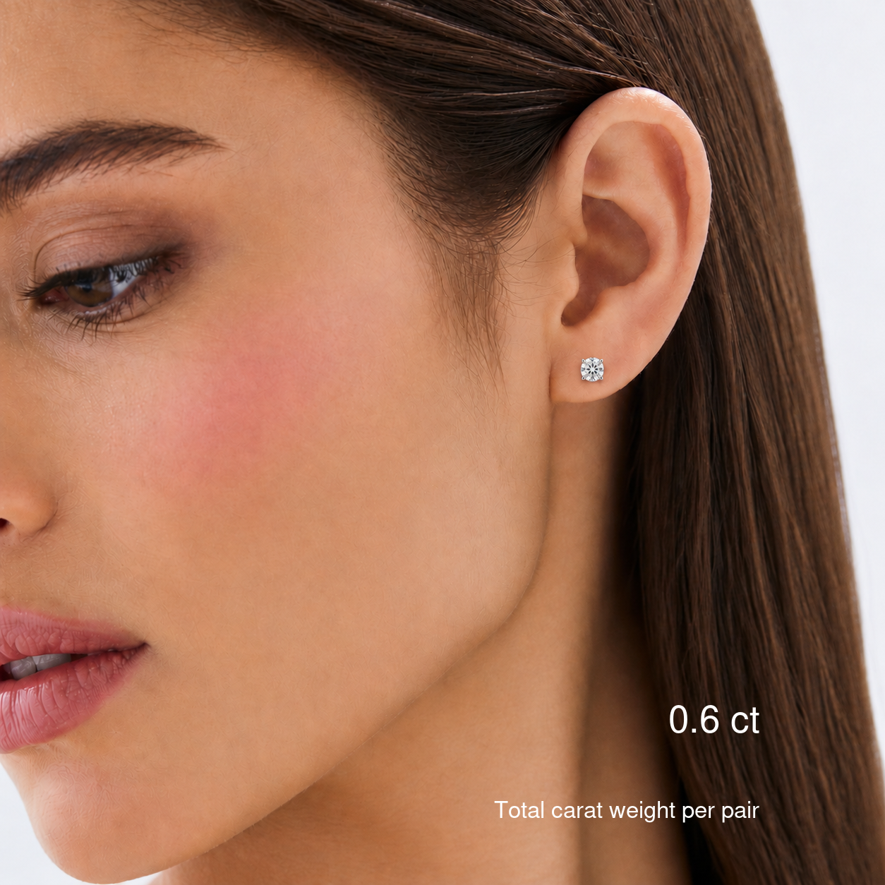 Round-cut moissanite stud earrings in white gold worn on a model, 0.6 ct total carat weight per pair.