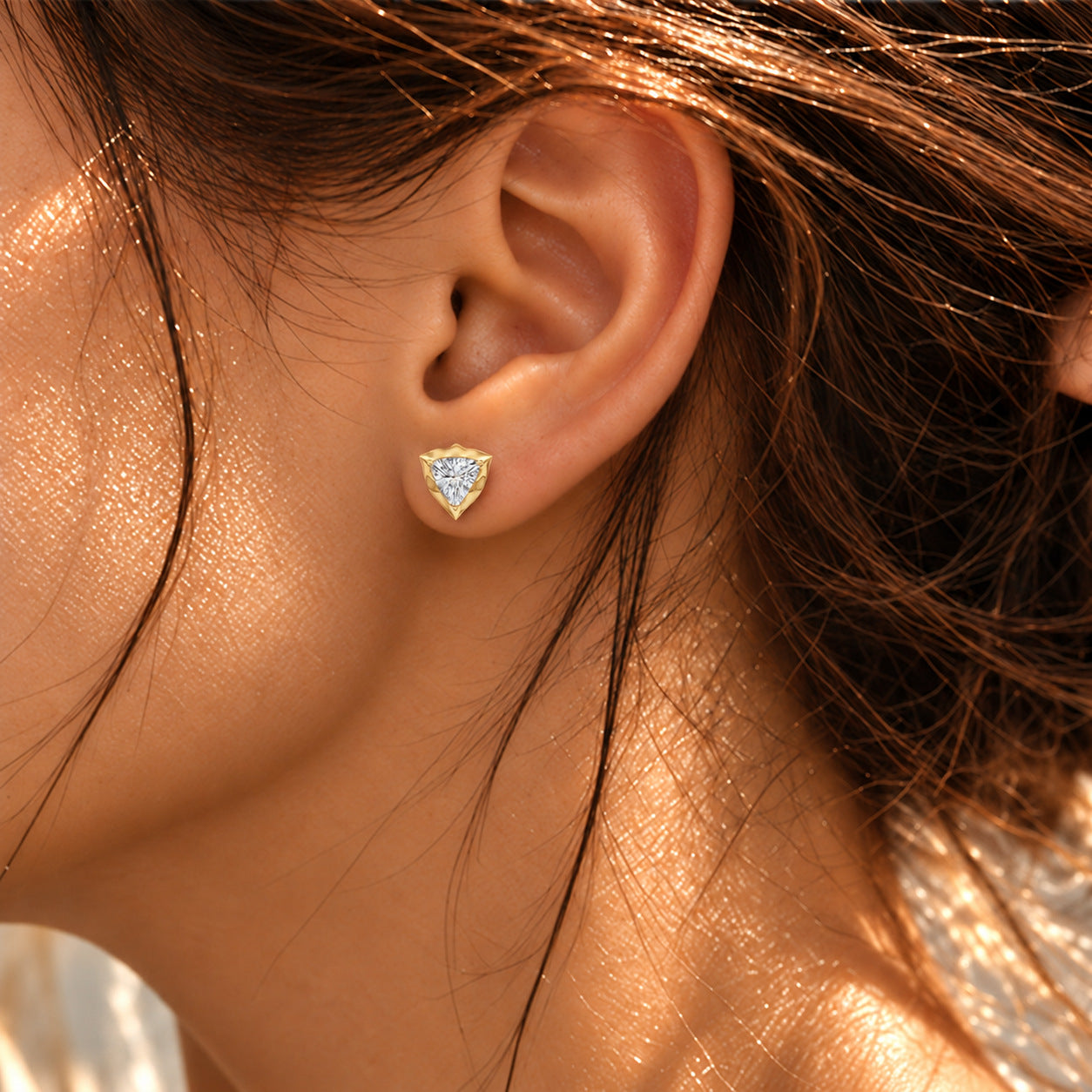 Close-up of a model wearing a trillion-cut moissanite bezel-prong stud earring in 18k yellow gold vermeil.