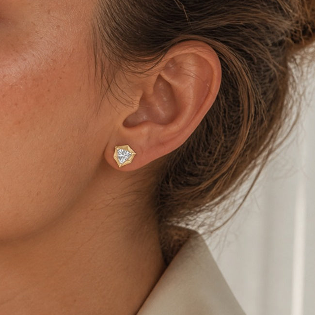Trillion-cut moissanite bezel-prong stud earrings in yellow gold vermeil, ear close-up.